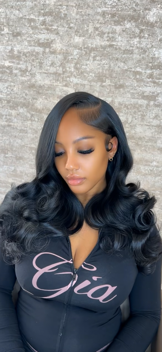 Woman with styled hair wearing a black top with 'Gia' printed on it against a textured wall.